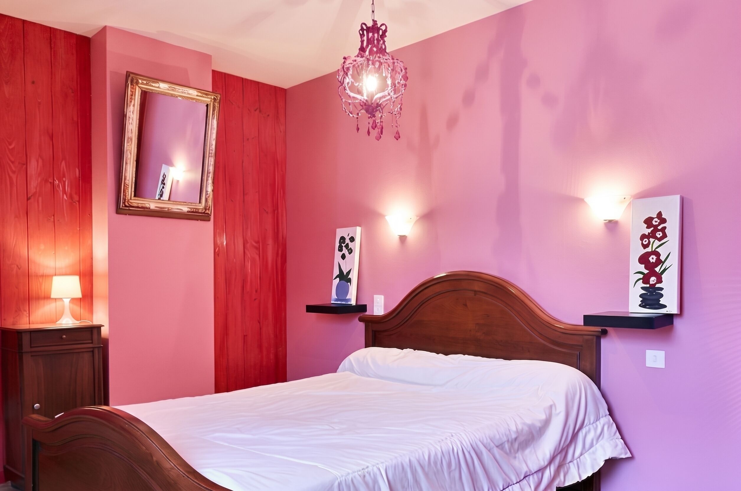 Ein Schlafzimmer mit einem hölzernen Bett, einem Spiegel, einer Chandelierleuchtre und Wandbildern.