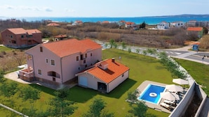 Una amplia casa de dos plantas con tejado de tejas rojas, piscina y vista al mar.