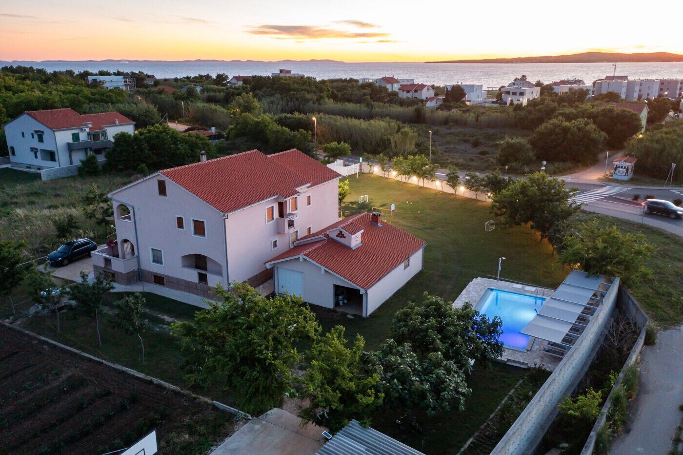 A residential area with houses, a swimming pool, and a view of the sea at sunset.