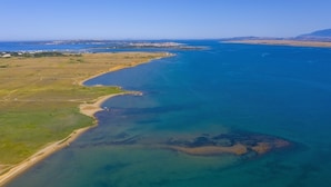 Vista aérea de una zona costera con playa, aguas azules cristalinas y formaciones terrestres a lo lejos.