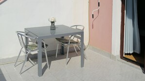 A balcony with a table and chairs, an air conditioning unit, and a door with curtains.