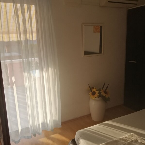 A bedroom with a bed, a window with sheer curtains, a mirror on the wall, and a vase with sunflowers. - Apartment in Privlaka with Seaview, Terrace, Air condition, WIFI (3591-2) (Privlaka)
