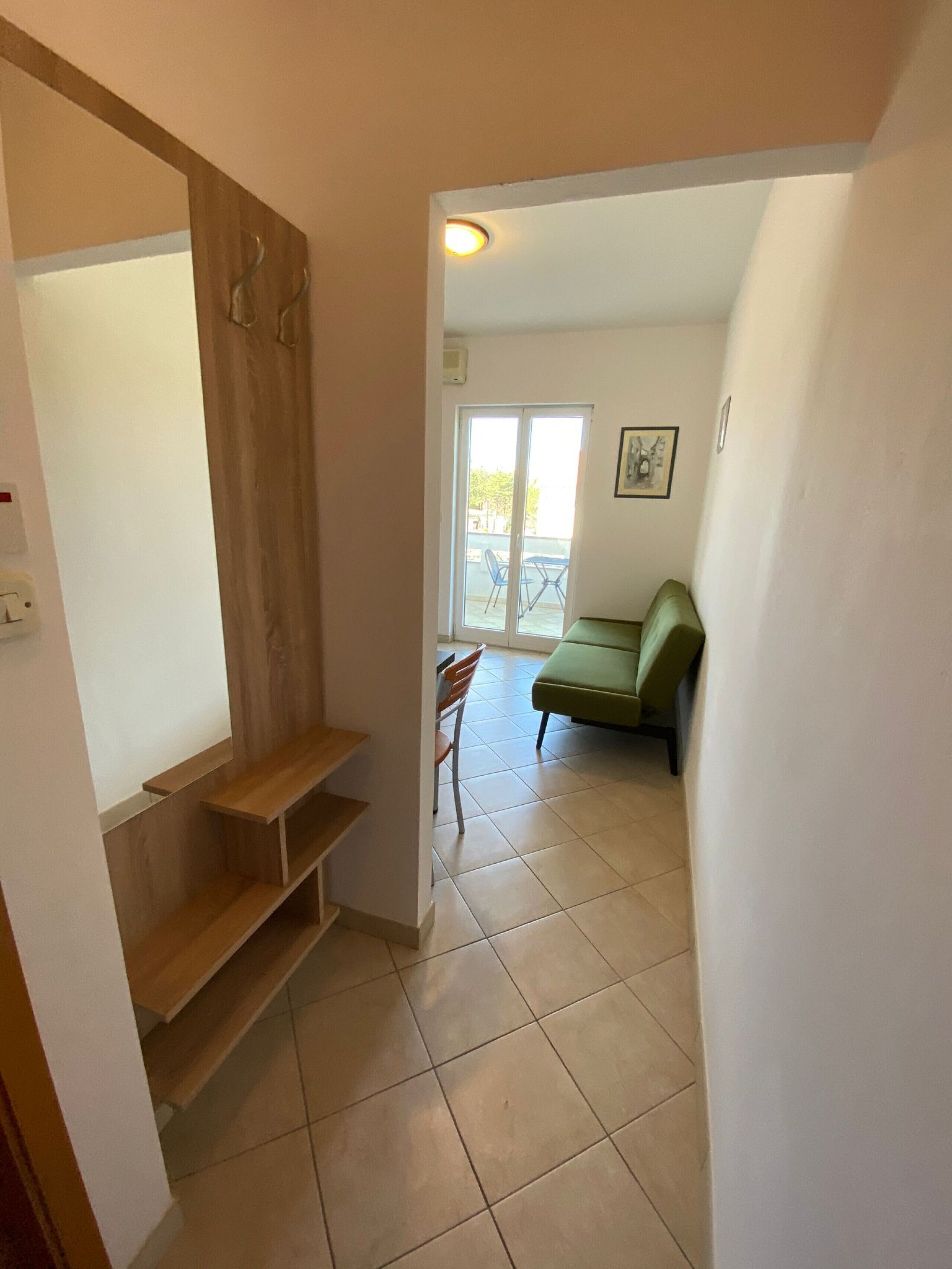 A hallway with a wooden staircase, a green sofa, and a dining area with chairs and a table.