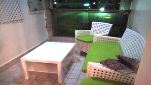 Ein kleiner Balkon mit einem weißen Tisch und zwei weißen Korbstühlen mit grünen Kissen.