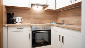 Una cocina compacta con armarios blancos, horno integrado, cafetera y lavabo.