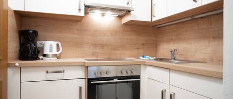 A compact kitchen with white cabinets, a built-in oven, a coffee maker, and a sink.