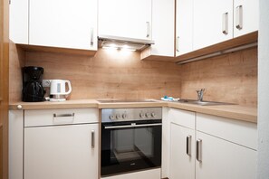 A compact kitchen with white cabinets, a built-in oven, a coffee maker, and a sink.