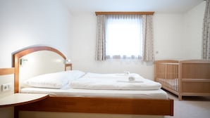 Un dormitorio con una cama de madera, cabecera de madera, mesita de noche, cuna y una ventana con cortinas.