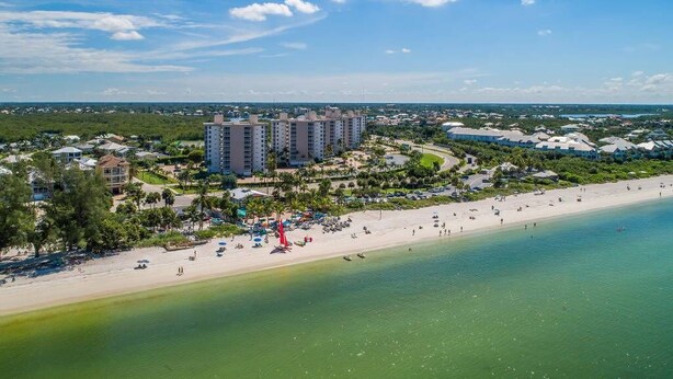 Un resort costero con villas frente a la playa, una playa de arena y un cielo azul despejado.