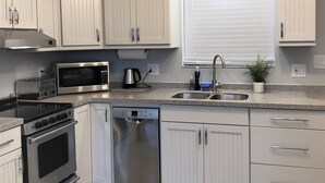 Una cocina moderna con armarios blancos, electrodomésticos de acero inoxidable, lavavajillas y un ventanal con persianas.