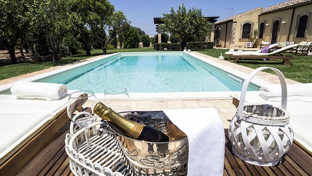 Un espace aménagé au bord de la piscine, avec une piscine à eau claire, des chaises longues et une bouteille de champagne dans un récipient décoratif.