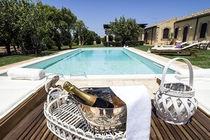 A poolside area with a clear pool, lounge chairs, and a bottle of champagne in a decorative container.