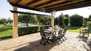 Une terrasse extérieure avec une pergola, une table à manger, des chaises et une piscine en arrière-plan.