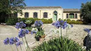 Un bâtiment avec un toit recouvert de tuiles, une porte verte et un jardin où poussent des fleurs bleues.