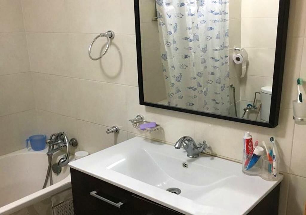 A bathroom with a white sink, a mirror, a towel ring, a shower, and a toilet.