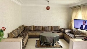 A living room with a sectional sofa, a small round table, and a television. - Nice apartment in residence Zina Sidi Bouzid 4306 (Sidi Bouzid)