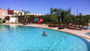 A swimming pool with a person in the water, surrounded by a playground with slides and a bridge. - Nice apartment in residence Zina Sidi Bouzid 4306 (Sidi Bouzid)