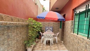 A small outdoor pool area with a table and chairs under a striped umbrella, surrounded by stone walls and potted plants. - Nice apartment in residence Zina Sidi Bouzid 4306 (Sidi Bouzid)