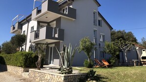 Une maison moderne à deux étages, dotée d’un balcon, d’un mur de soutènement en pierre et d’une pelouse avec une chaise.