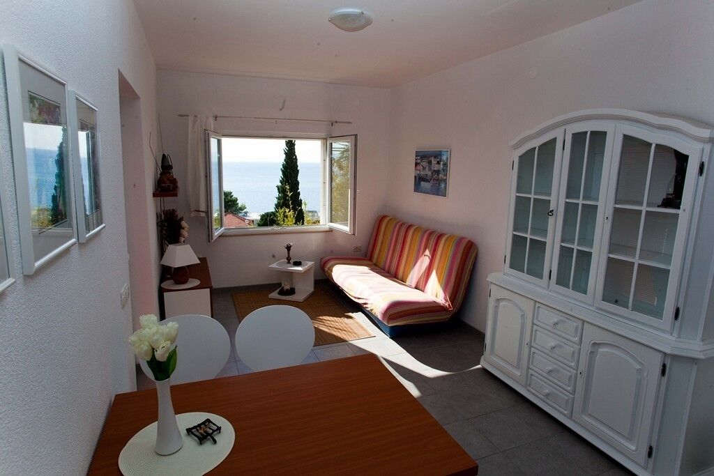 Una habitació acollidora amb un sofà, una taula de dinar amb cadires, un armari i una finestra que ofereix vistes al mar.