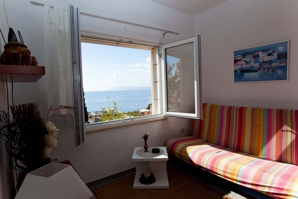 A room with a window overlooking the sea, a colorful striped sofa, and a small table with a vase.