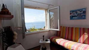 A room with a window overlooking the sea, a colorful striped sofa, and a small table with a vase. - Apartment in Podgora with Seaview, Terrace, Air condition, WIFI (849-1) (Podgora)