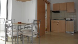 Et køkken med spisebord og stole, en mikrobølgeovn på en hylde samt træskabe.