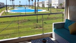 En balkong med utsikt över en swimmingpool, palmer och en byggnad i bakgrunden.