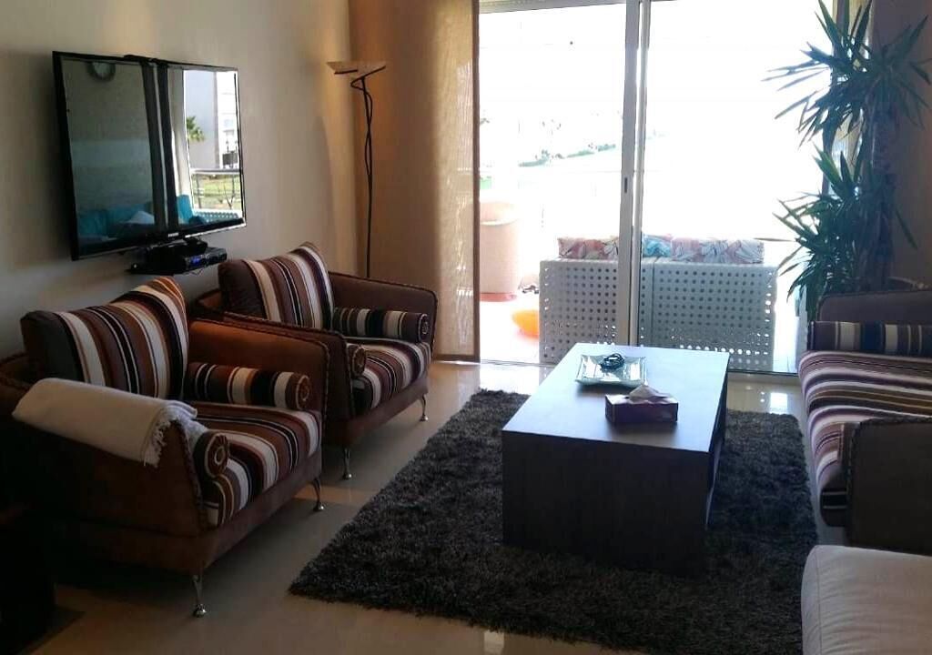 A living room with striped sofas, a coffee table, a flat-screen TV, and a large window with a view of the outdoors.