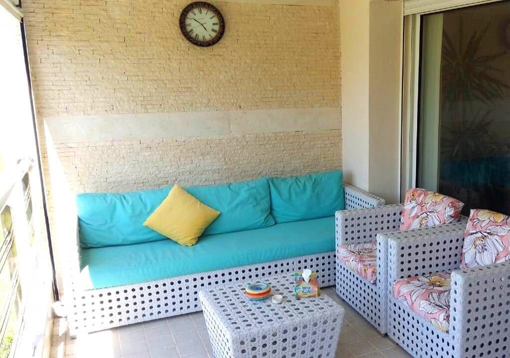 Un balcón con un sofá y dos sillones, una mesita pequeña y un reloj en la pared.