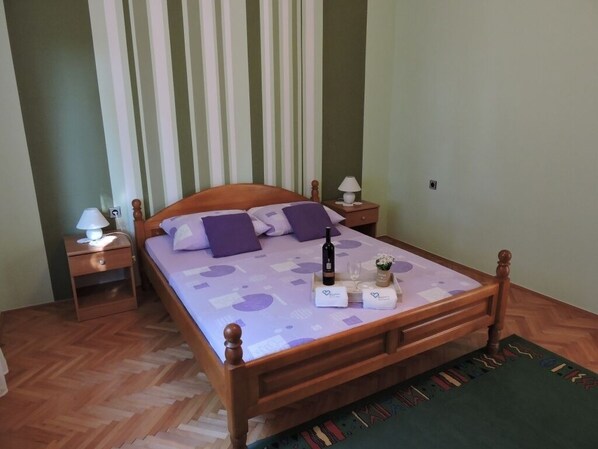 A neatly made bed with a wooden frame, a nightstand with a lamp, and a bedside table with a bottle and glasses. - Apartment in Biograd na Moru with Terrace, Air condition, WIFI, Dishwasher (4269-1) (Biograd na moru)