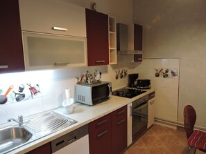 Compact kitchen with stainless steel sink, gas stove, and oven, complete with a range hood and small countertop area.