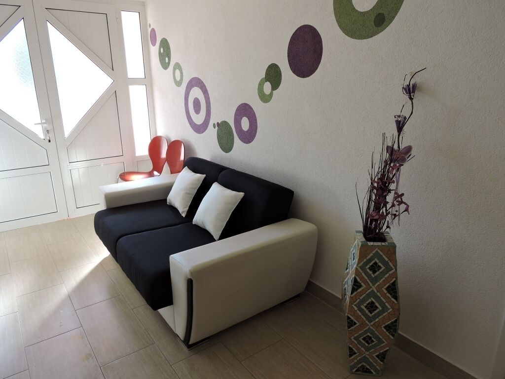 Un soggiorno moderno con un divano, una parete decorativa con motivi astratti e un vaso con piante.