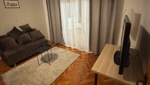 Een woonkamer met een bank, een tafeltje, een televisie en een raam met gordijnen.