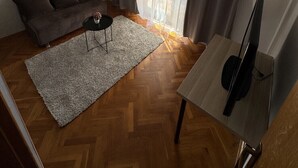 Een woonkamer met een bank, een kleine tafel, een televisie en een raam met gordijnen.