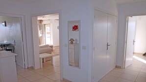 A spacious living area with a sofa, a small table with a lamp, and a door leading to another room.
