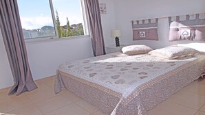 A bedroom with a large bed, a nightstand, a lamp, and a view of the outside.