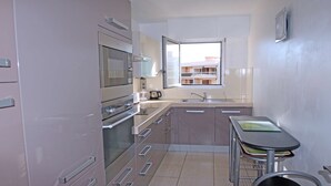 A compact kitchen with stainless steel appliances, a window with a view of buildings, and a small dining area with stools.