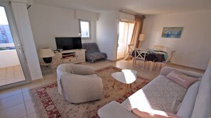 Un salon comprenant un canapé, un fauteuil, un téléviseur et un coin repas avec des chaises et une table.