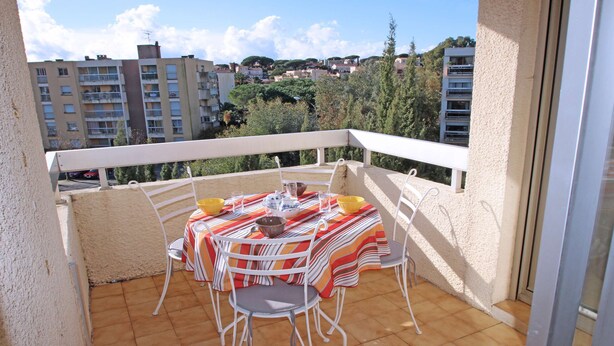 A balcony with a table set for two, chairs, and a view of surrounding buildings.