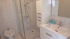 Une salle de bain avec une douche à parois de verre, un lavabo blanc avec un miroir et un bidet.