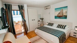 Een slaapkamer met een bed, nachtkastjes, een bureau, een stoel, een raam met gordijnen, een schilderij aan de muur en uitzicht op de omgeving.