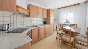 A modern kitchen with wooden cabinets, a black stove, and a dining area with a table and chairs. - Apartment in Sukošan with Seaview, Terrace, Air condition, WIFI (3495-3) (Sukošan)
