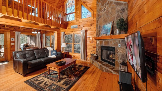 Ein Holzblockhaus-Interieur mit Kamin aus Stein, Holzböden, einem Ledersofa und einem Essbereich.