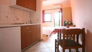 A compact kitchen with wooden cabinets and a white countertop. There is a dining area with a table and chairs, and a window with curtains. - Studio apartment in Poreč with Balcony, Air condition, WIFI (3794-6) (Porec)