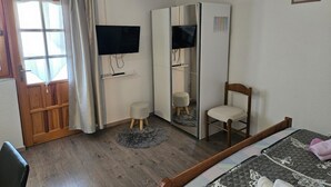 Quarto com cama, cadeira, guarda-roupa, televisão e janela com cortinas.