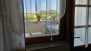 Janela com cortinas leves, um vaso com planta no parapeito e vista para o verde lá fora.