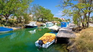 Um rio calmo com barcos atracados na margem, cercado por árvores e edifícios ao fundo.