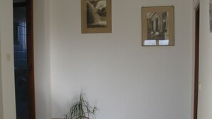 Un couloir avec un sol carrelé, une plante en pot et deux tableaux encadrés accrochés au mur.