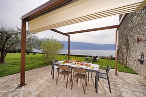 An outdoor dining area with a table set for a meal, overlooking a body of water and mountains.